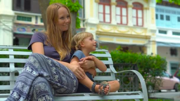 Jovem e seu filho se sentam em um banco em uma praça em uma parte antiga da cidade de George, Penang, Malásia — Vídeo de Stock