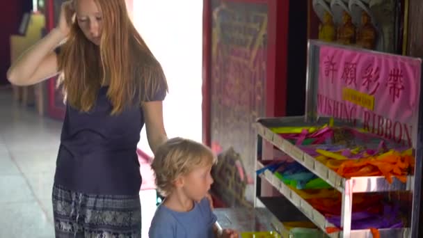 A young woman and her little son visit Kek Lok Si Buddhist temple and write wishes on a colored textile — Stock Video