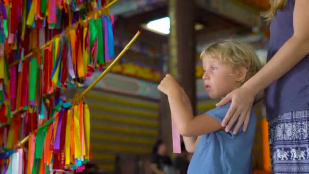 A young woman and her little son visit Kek Lok Si Buddhist temple and write wishes on a colored textile and hang it on the wish tree — Stock Video