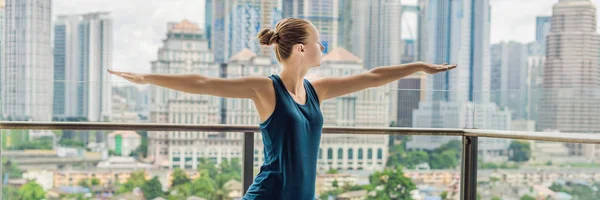 Young woman is practicing yoga in the morning on her balcony with a panoramic view of the city and skyscrapers. BANNER, long format