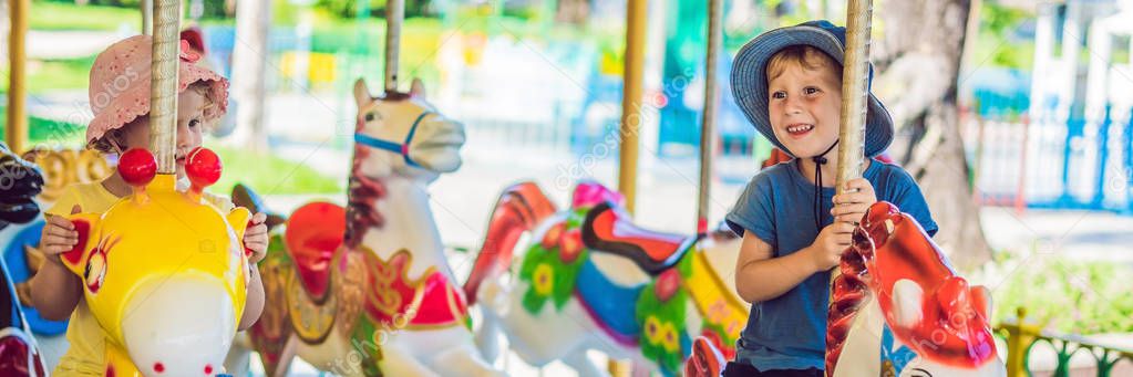Cute little boy and girl enjoying in funfair and riding on colorful carousel house. BANNER, long format