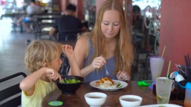 Sevimli küçük çocuk genç kadınla Asya yemekleri masada yemek.