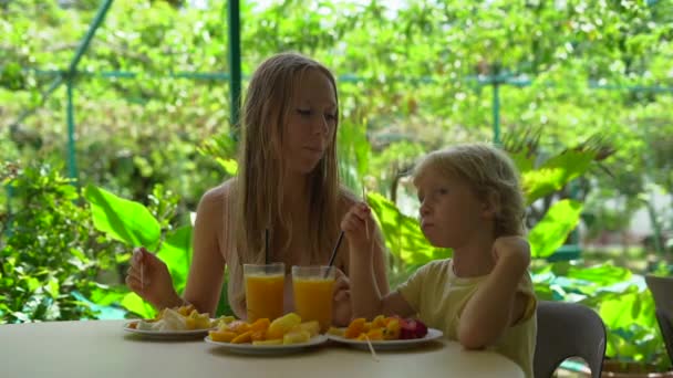 年轻妇女与小男孩吃热带水果和饮用的果汁在桌上自然背景 — 图库视频影像