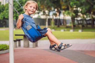 Komik çocuk çocuk açık sahada zinciri salıncak ile eğleniyor. Sıcak gününde sallanan çocuk. Etkin boş çocuklarla. Casual renkli okul çocuk kıyafetleri giyen çocuk.