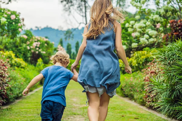 Anne ve oğlu çiçek açan bahçede koşturup. Mutlu aile yaşam tarzı kavramı.