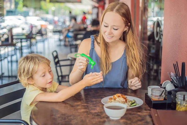 Anne ve oğlu yıkama el dezenfektanı kullanarak bir kafede yemeden önce jel.