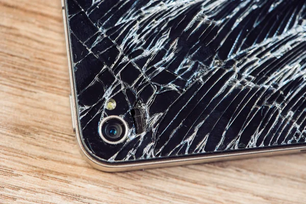 Smartphone display with broken glass on a wodden table.