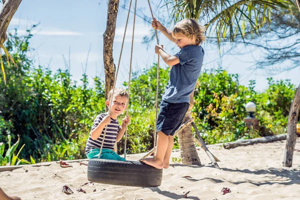 Dos niños rubios divirtiéndose en el columpio en la costa arenosa tropical — Foto de Stock