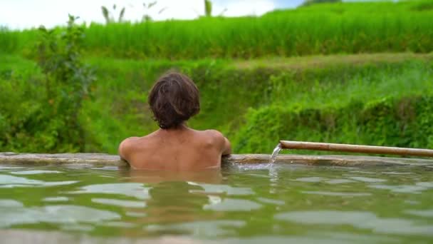 バリ島の野生の温泉浴場で座っている若い男の背面図 — ストック動画