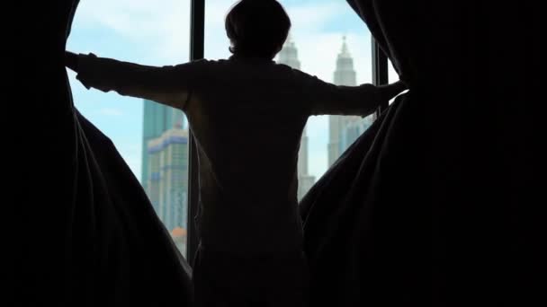 Superslowmotion shot van een silhouet van een succesvolle, rijke man openen de gordijnen van een venster met uitzicht op het centrum van de stad met wolkenkrabbers — Stockvideo