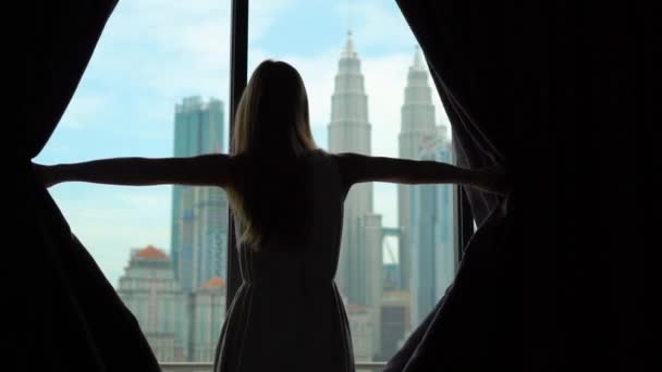 Superslowmotion disparo de una silueta de una mujer rica de éxito abriendo las cortinas de una ventana con vistas al centro de la ciudad con rascacielos . — Vídeos de Stock