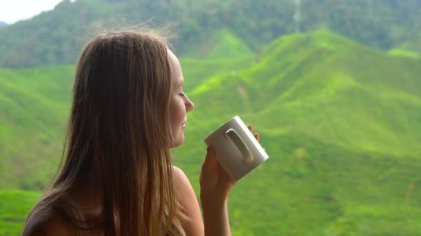 Снимок медленного движения молодой женщины, сидящей в кафе с видом на горные чайные террасы и пьющей чай — стоковое видео