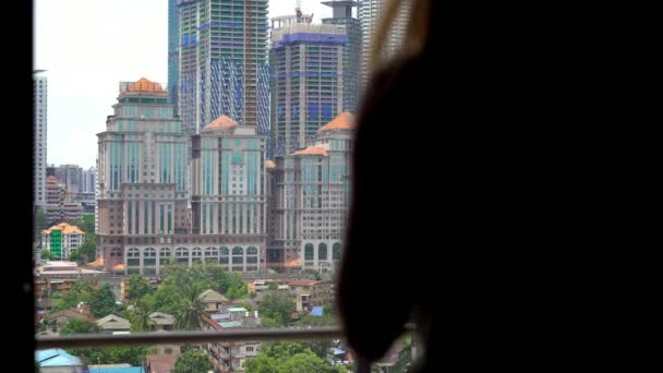 Jonge vrouw komt naar een balkon van haar appartement met uitzicht op een vol skyscrappers centrum van de stad en's ochtends koffie drinkt — Stockvideo