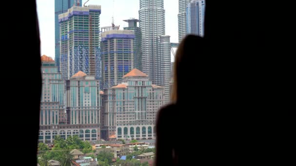 Jeune femme vient à un balcon de son appartement avec une vue sur un centre-ville plein de gratte-ciel et boit du café du matin — Video