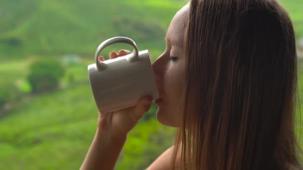 Jonge vrouw zitten in een cafe met uitzicht op de hooglanden thee plantattions en het drinken van thee. — Stockvideo