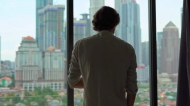 bir adam geliyor ve gökdelenler ile şehir merkezine bakan bir pencere perdeleri silüeti