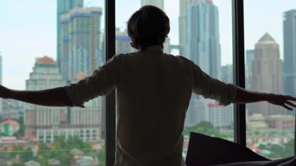 Silhouette of a successful rich man opening the curtains of a window overlooking the city center with skyscrapers — Stock Video