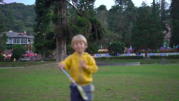 Slowmotion πυροβολισμό από ένα μικρό αγόρι, κάνοντας ένα μεγάλο σαπούνι φυσαλίδες σε ένα πάρκο — Αρχείο Βίντεο