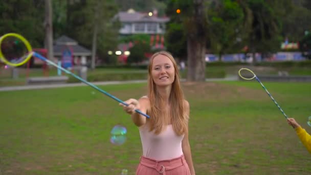Медленный снимок молодой женщины, делающей большие мыльные пузыри в парке — стоковое видео