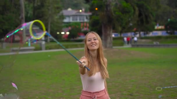 Slowmotion tiro de uma jovem mulher fazendo um grande bolhas de sabão em um parque — Vídeo de Stock