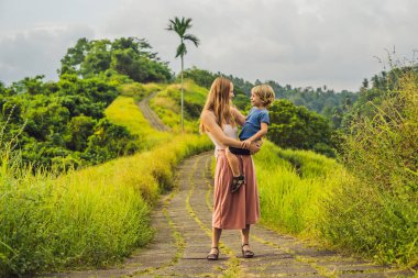 Anne ve her diğer ve gülümseyerek, bakarak oğlu Campuhan Ridge yürümek, Bali