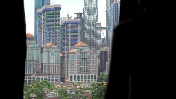 Молодой человек выходит на балкон своей квартиры с видом на центр города, полный небоскребов и пьет свой утренний кофе — стоковое видео