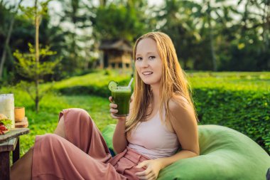 Young Woman with Fresh Green Vegetable Juice sitting outdoors in lush greenery