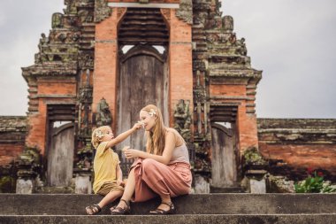 Anne ve oğlu geleneksel balinese adımda oturan hindu tapınağı Taman Ayun Mengwi, Bali, Endonezya.
