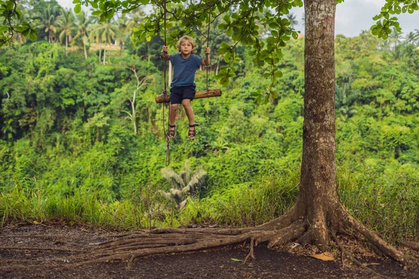 バリ島 インドネシアのヤシの木と熱帯林でのスイングの小さな男の子 — ストック写真