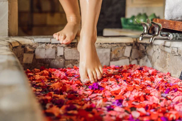 Feet of woman walking in spa bath with petals of tropical flowers