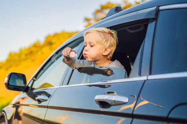 Boy blowing bubbles in car window in trip