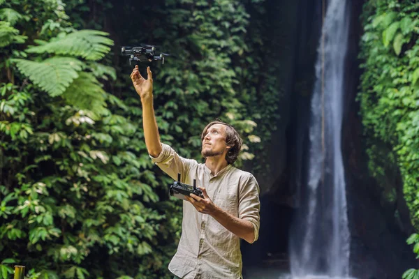 熱帯の植物と滝の背景でドローンを制御する男 — ストック写真