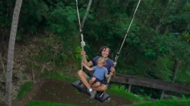 Genç bir adam ve oğlu tropikal bir uçuruma büyük salıncakta sallanan Slowmotion atış
