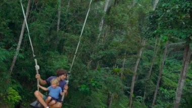 Genç bir adam ve oğlu tropikal bir uçuruma büyük salıncakta sallanan Slowmotion atış