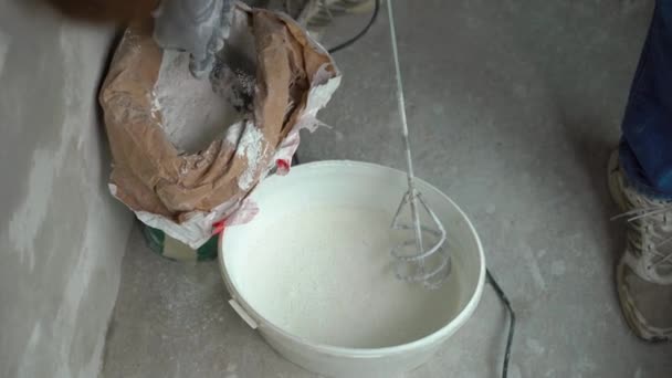 Ein junger Maler knetet Kitt mit Wasser in einem Eimer mit einem Handmixer für den Mischbau — Stockvideo