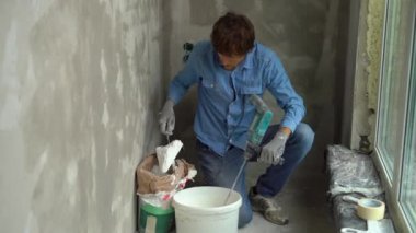 Genç bir erkek ressamın macun karışımları oluşturmak için bir el Mikser kullanarak bir kova su ile kneads