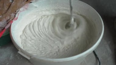 Genç bir erkek ressamın resmini Slowmotion macun karışımları oluşturmak için bir el Mikser kullanarak bir kova su ile kneads