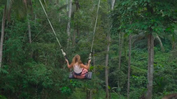 Медленный снимок молодой женщины, качающейся на больших качелях над скалой в тропиках — стоковое видео