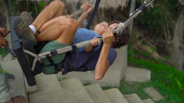 Медленный снимок молодого человека и его сына, качающихся на больших качелях над скалой в тропиках — стоковое видео