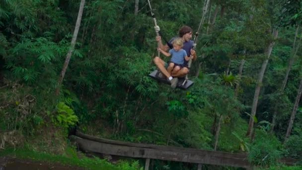 Fotografía en cámara lenta de un joven y su hijo balanceándose en un gran columpio sobre un acantilado en los trópicos — Vídeos de Stock