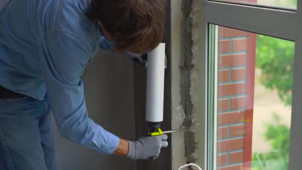 Filmagem em câmara lenta de um jovem instalando uma janela de plástico. Instalador preenche as costuras com espuma — Vídeo de Stock