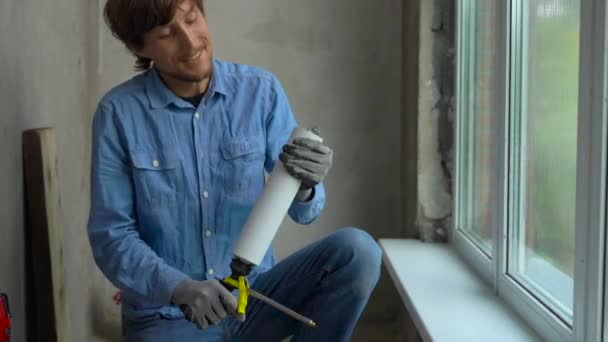 Plan au ralenti d'un jeune homme installant une fenêtre en plastique. Installateur secoue le ballon avec une mousse de montage — Video