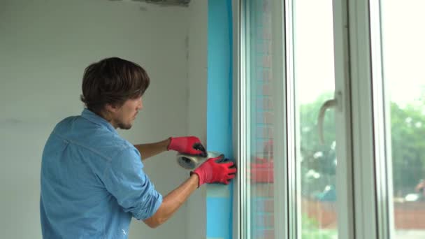 A young man installing plastic window. Installer fills the slope of plastic window with a mounting foam — Stock Video