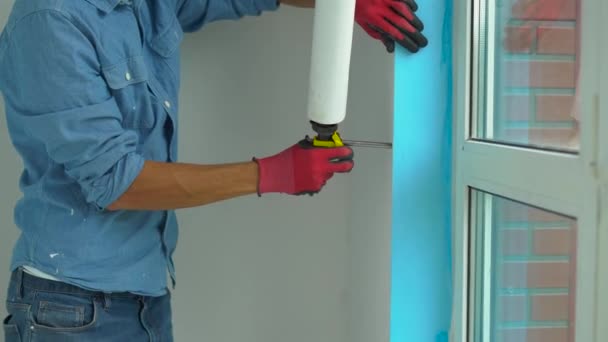 A young man installing plastic window. Installer fills the slope of plastic window with a mounting foam — Stock Video