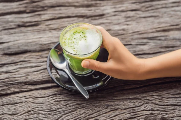 matcha latte ahşap masa üzerinde bardak tutan el
