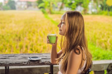 Genç kadın pirinç terasları Bali, Endonezya yakınındaki kafe verandada Matcha latte içmek