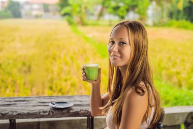 Genç kadın pirinç terasları Bali, Endonezya yakınındaki kafe verandada Matcha latte içmek