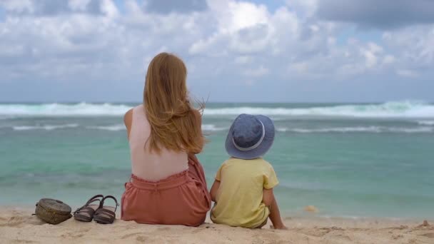 Slow motion tiro de uma jovem mulher e seu filho sentado uma areia na praia de Melasti na ilha de Bali — Vídeo de Stock