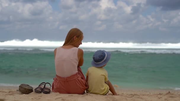 Strzał slowmotion młoda kobieta i jej syn siedzi piasku w Melasti Beach na wyspie Bali — Wideo stockowe