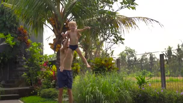 Сверхнизкий кадр отца бросает своего сына в бассейн в тропиках — стоковое видео